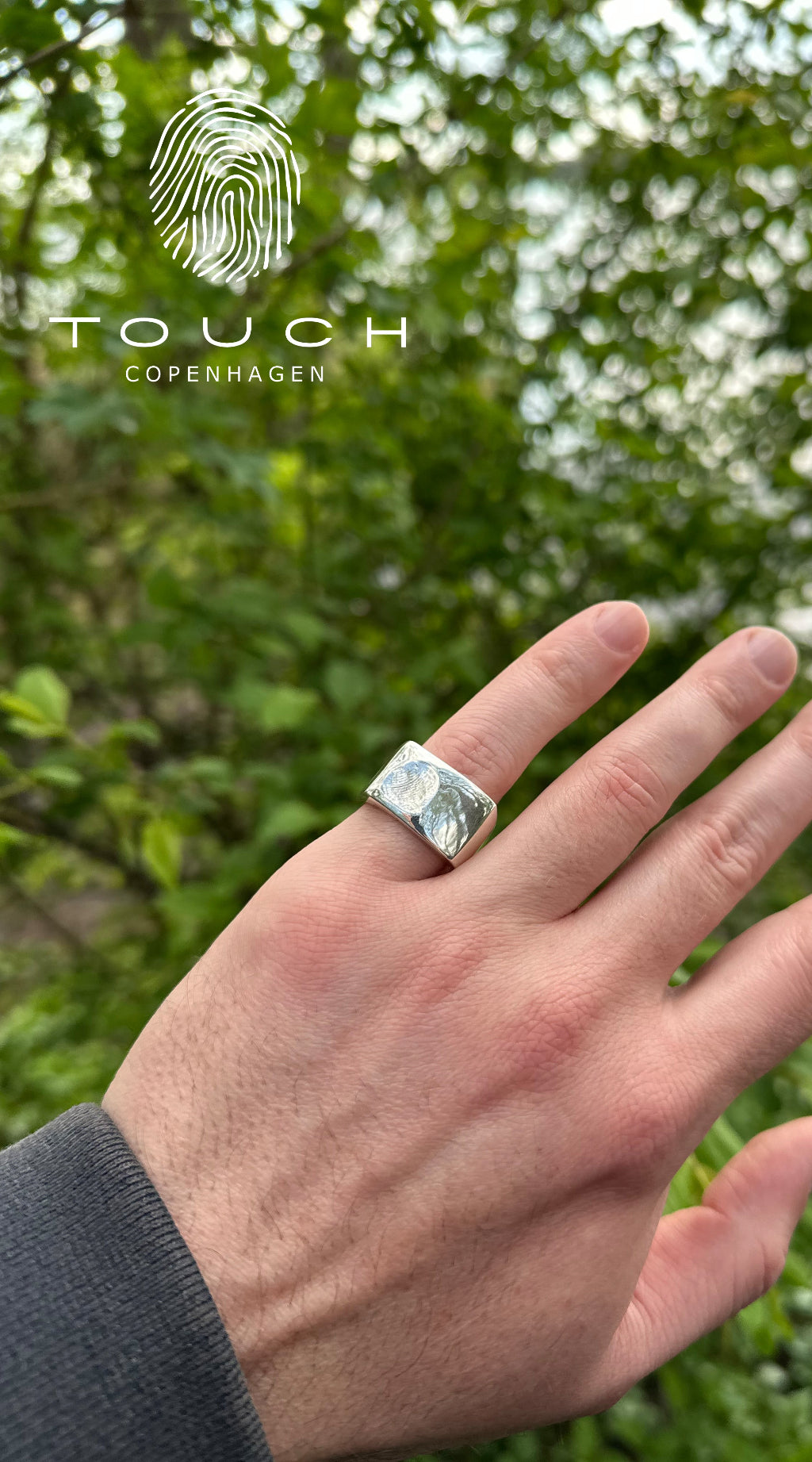 Max sølvring fra Touch Copenhagen -med fingeraftryk af barn vist på hånd, med natur baggrund.